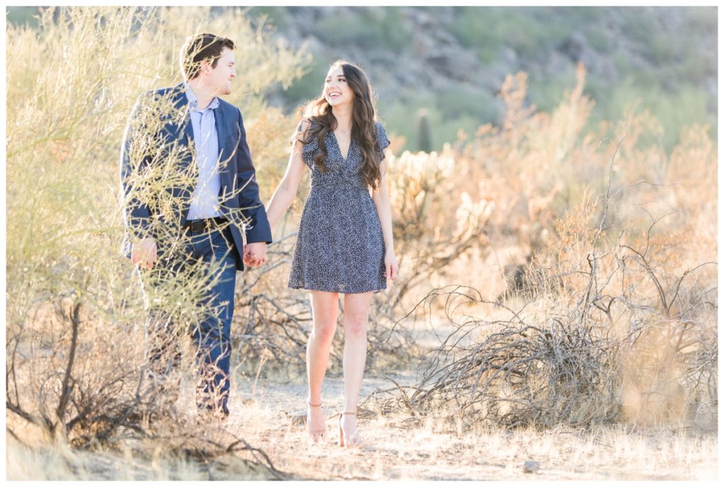 A man and a woman each with dark hair wearing blue tones kiss in the desert in Scottsdale for their engagement photos