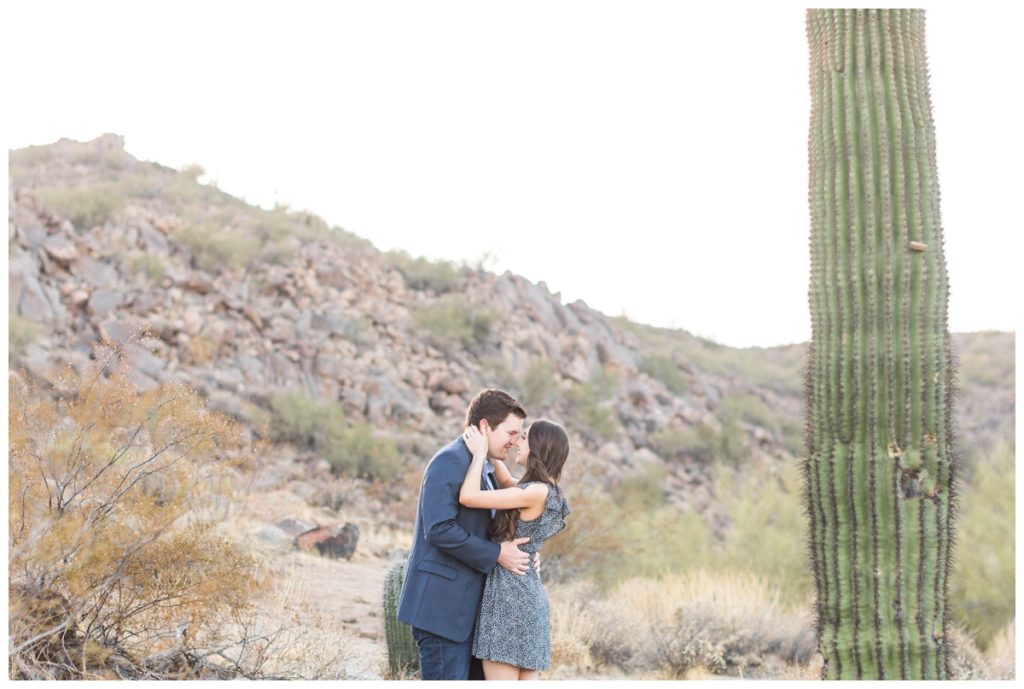 A man and a woman each with dark hair wearing blue tones kiss in the desert in Scottsdale