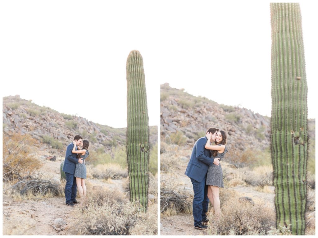 A man and a woman each with dark hair wearing blue tones kiss in the desert in Scottsdale for their engagement photos