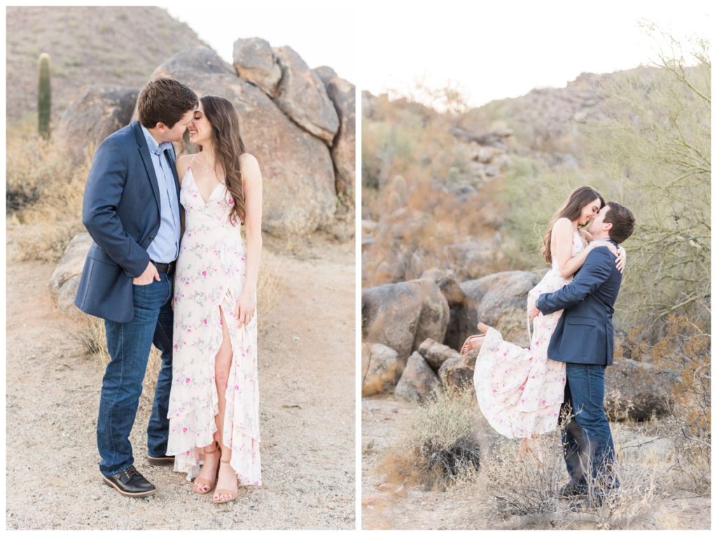 A man and a women with dark hair pose for their engagement photos while he picks her up. He's in a blue suit jacket and she's in a light pink floral dress. 