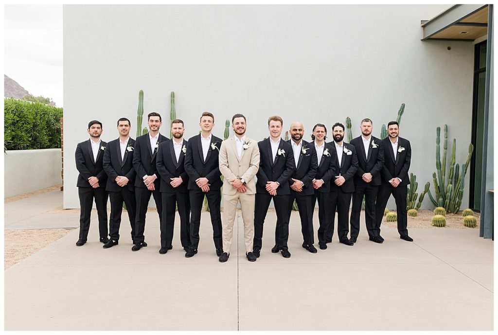 Groomsmen in black suits surround a groom in a khaki suit on his wedding day